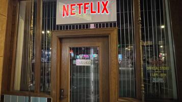Een gebouw met een bordje met de tekst 'NETFLIX' boven de ingang, een gesloten bord op de deur en een raam met een rasterpatroon.