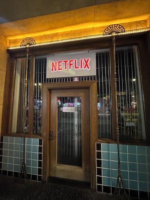 Een gebouw met een bordje met de tekst 'NETFLIX' boven de ingang, een gesloten bord op de deur en een raam met een rasterpatroon.