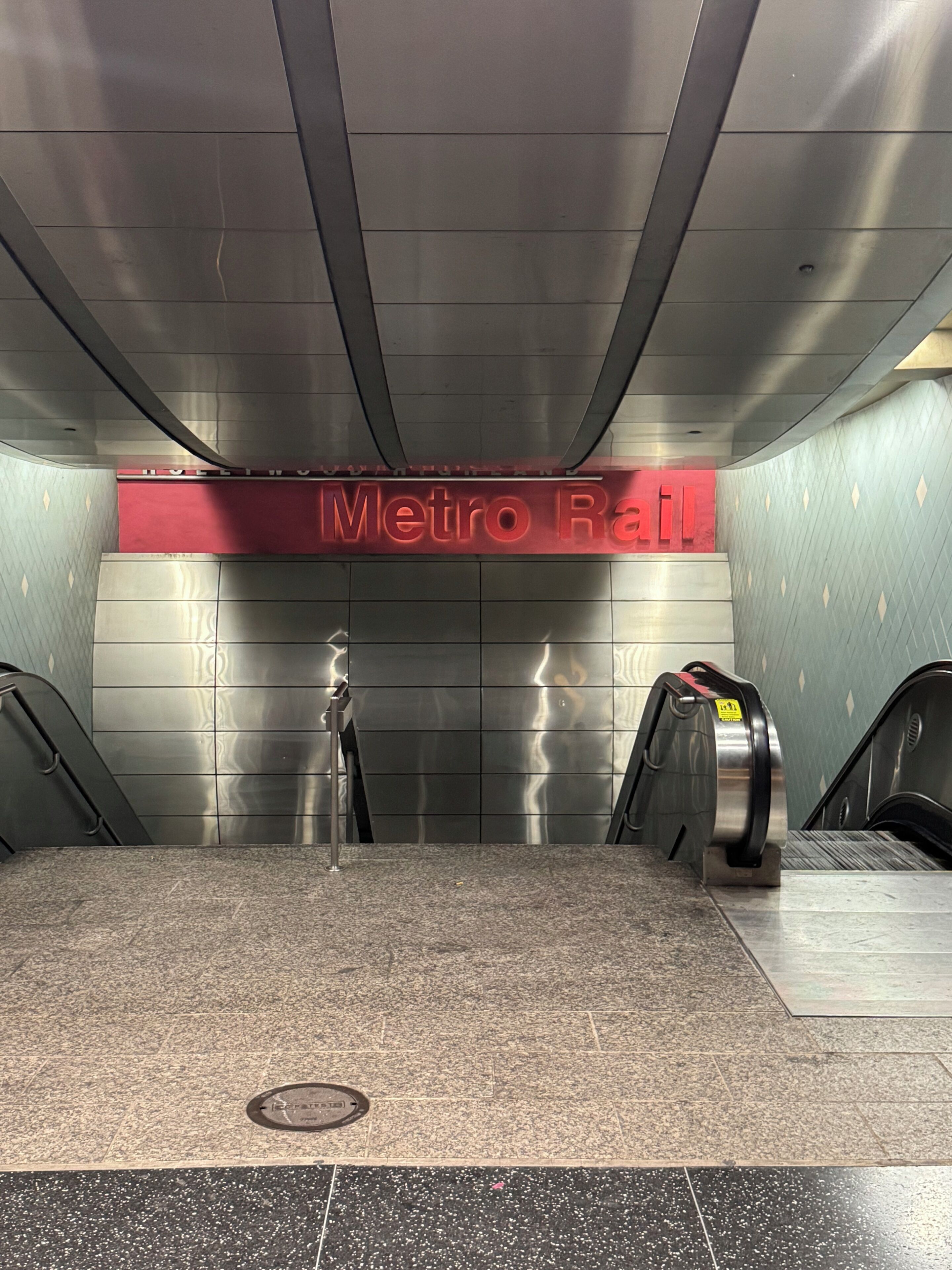 Eine Metro-Bahnhofstation mit einem roten Schild, Rolltreppen und einem gefliesten Boden.