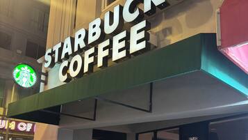Een Starbucks Coffee winkel met een groot verlicht bord, een duidelijke ingang en een scooter die er buiten geparkeerd staat.