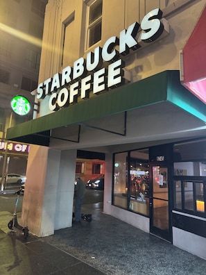 Een Starbucks Coffee winkel met een groot verlicht bord, een duidelijke ingang en een scooter die er buiten geparkeerd staat.