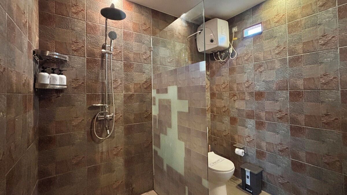 Un baño con ducha de vidrio, inodoro y dispensador de jabón en la pared.