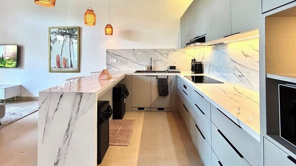 A modern kitchen with a marble countertop, built-in appliances, and pendant lighting. - Villa Exquise (Legian)