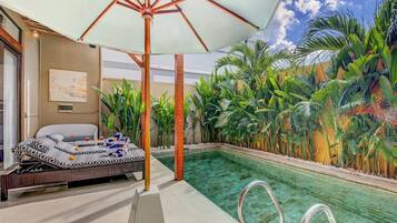 Zona de piscina con una silla de descanso, una sombrilla grande y exuberante vegetación tropical.