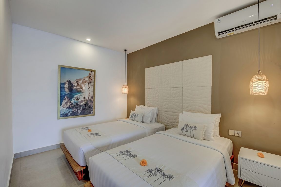 Une chambre d’hôtel avec deux lits, une grande tête de lit fixée au mur, un tableau et une table de chevet.