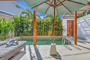 A pool area with a lounge chair and umbrella, surrounded by tropical plants. - Villa Exquise (Legian)