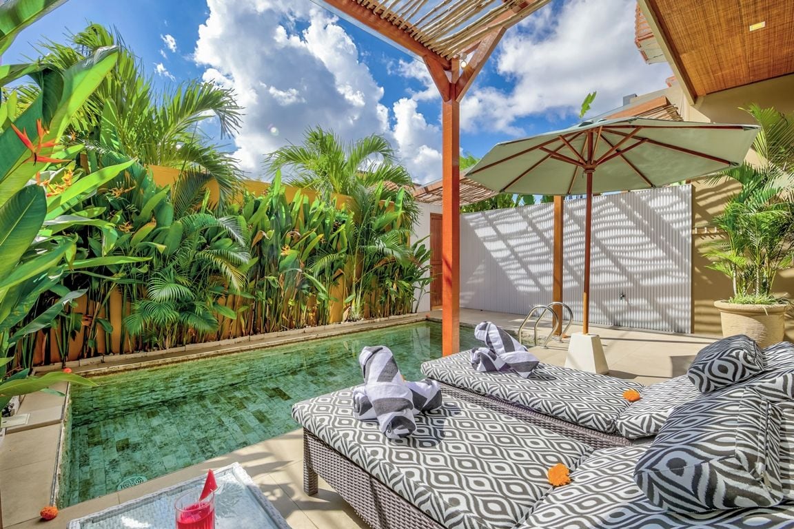 Ein Poolbereich mit Liegestuhl und Tisch, umgeben von üppiger tropischer Vegetation.