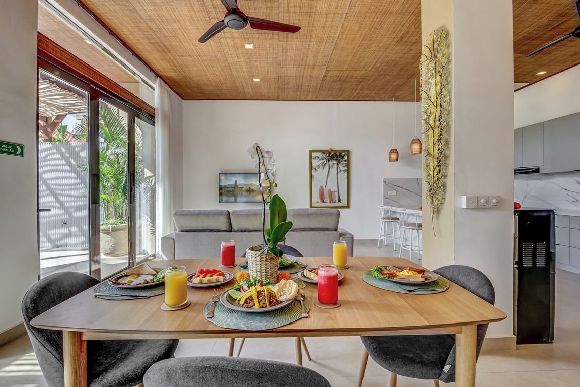 Un comedor con una mesa de madera preparada para una comida, un ventilador de techo y vistas al exterior.