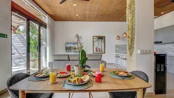 Un comedor con una mesa de madera preparada para una comida, un ventilador de techo y vistas al exterior.