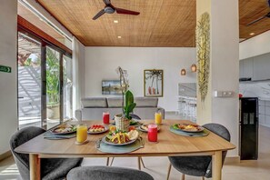 Un comedor con una mesa de madera preparada para una comida, un ventilador de techo y vistas al exterior.