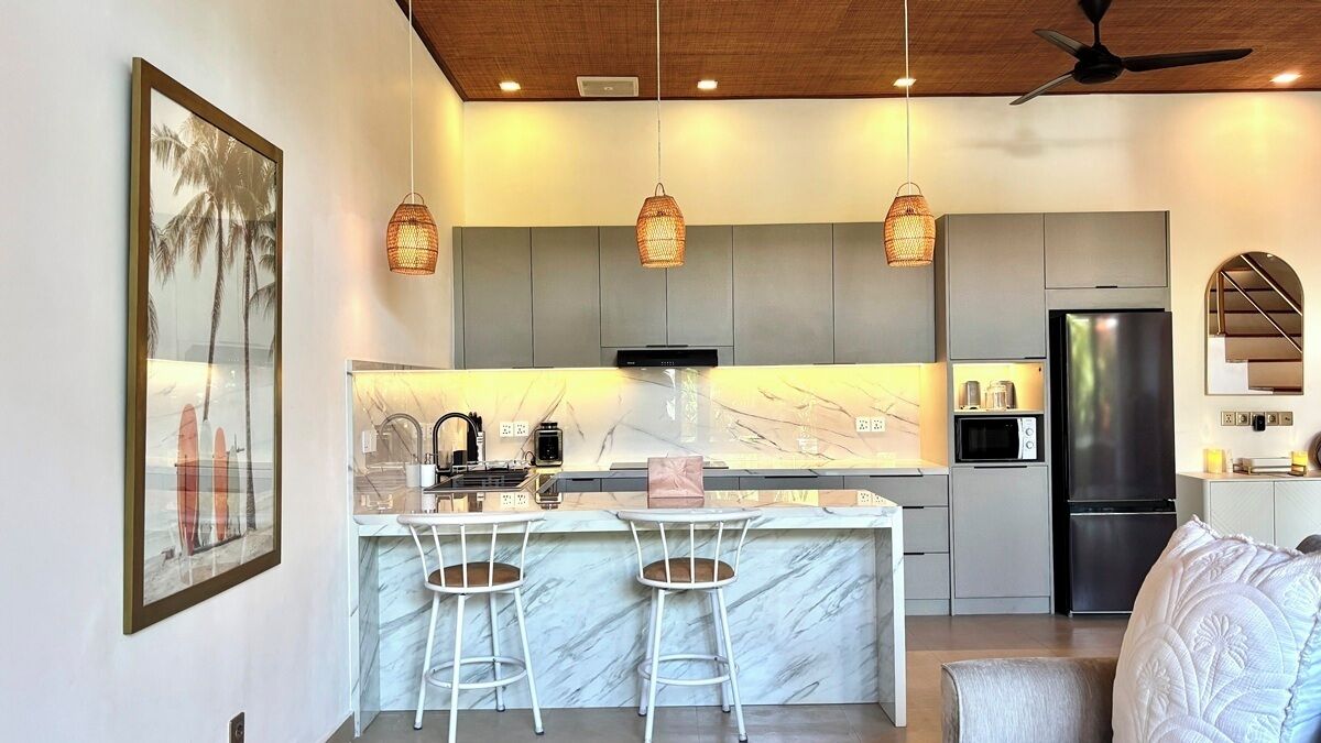 A modern kitchen with a marble countertop, two bar stools, a built-in oven, and a refrigerator.