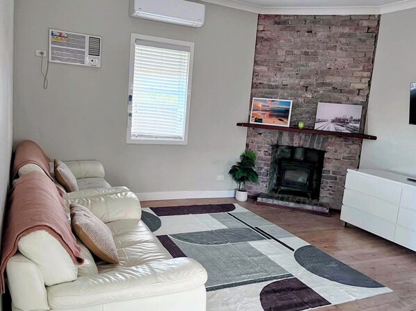 A living room with a white sofa, a fireplace, and a television on a white cabinet.