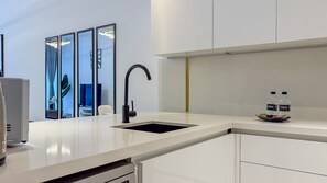 A modern kitchen with a white countertop, a black faucet, and a sink. There are two water bottles on the counter. - Full Burj Khalifa View, Central Dubai, Furnished (Dubai)