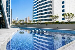 A modern swimming pool with clear blue water, surrounded by contemporary buildings and greenery. - Full Burj Khalifa View, Central Dubai, Furnished (Dubai)