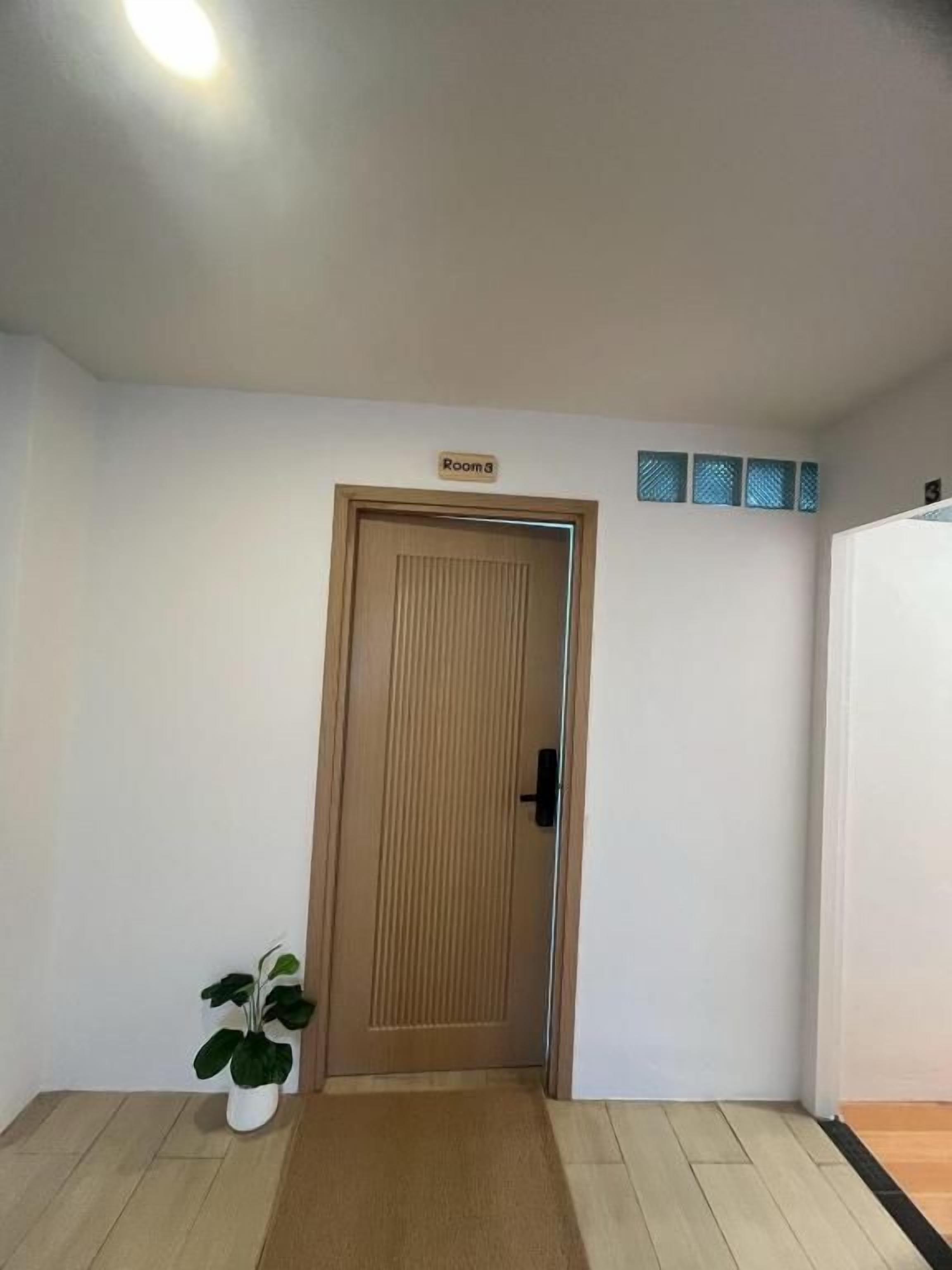 Ein Zimmer mit Holztür, einem kleinen Topfpflanzen und einem Schild mit der Aufschrift 'Zimmer 3'.