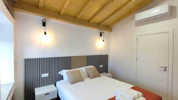 A hotel room with a bed, bedside tables, a wooden ceiling, and an air conditioning unit.