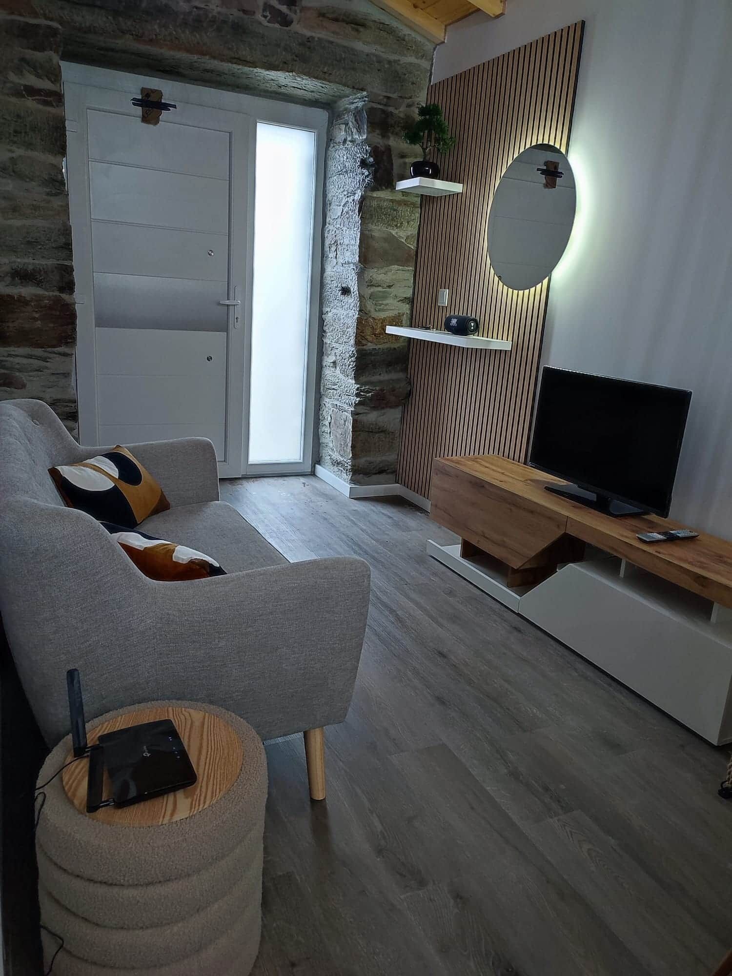 Una sala de estar moderna con un sofá gris, un mueble de televisión de madera y una pared de piedra.