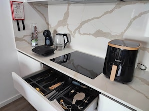 A kitchen with a built-in stove, a coffee maker, and a drawer with utensils.