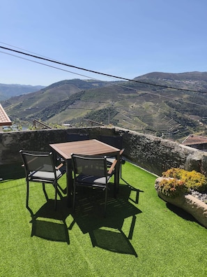 A terrace with a table and chairs, overlooking terraced fields and hills.