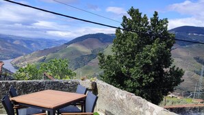 Una terrazza esterna con tavolo e sedie, circondata da un muro in pietra e vista su dolci colline.