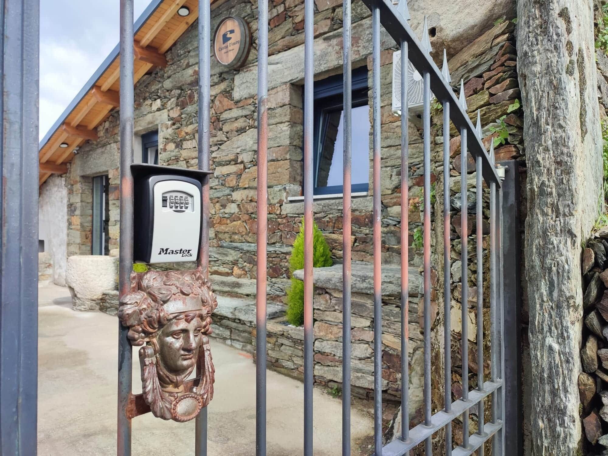 A stone building with a metal gate, a Master Lock device, and a rustic door handle.