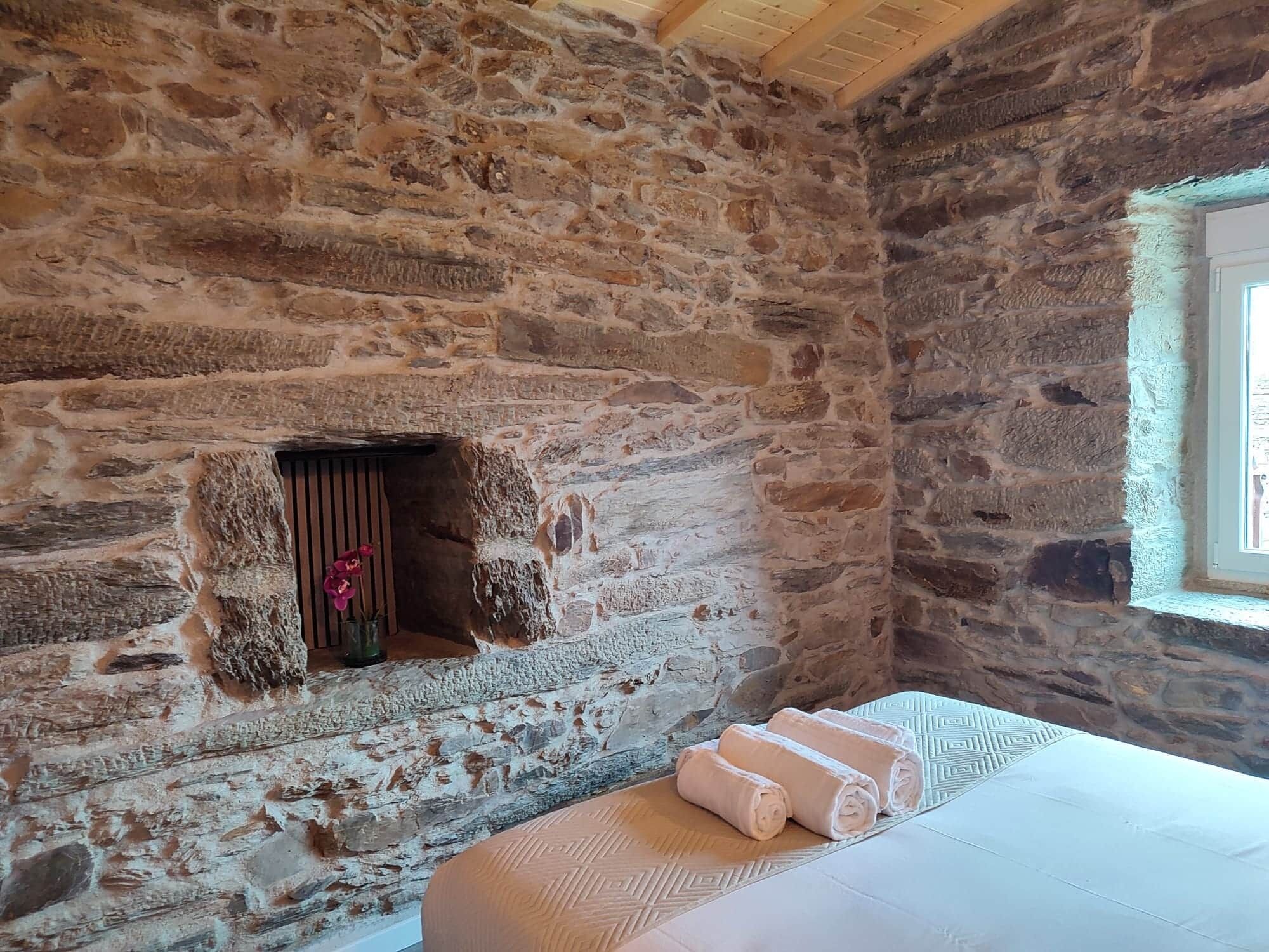 A stone-walled room with a small window, a bench, and a towel on the bench.