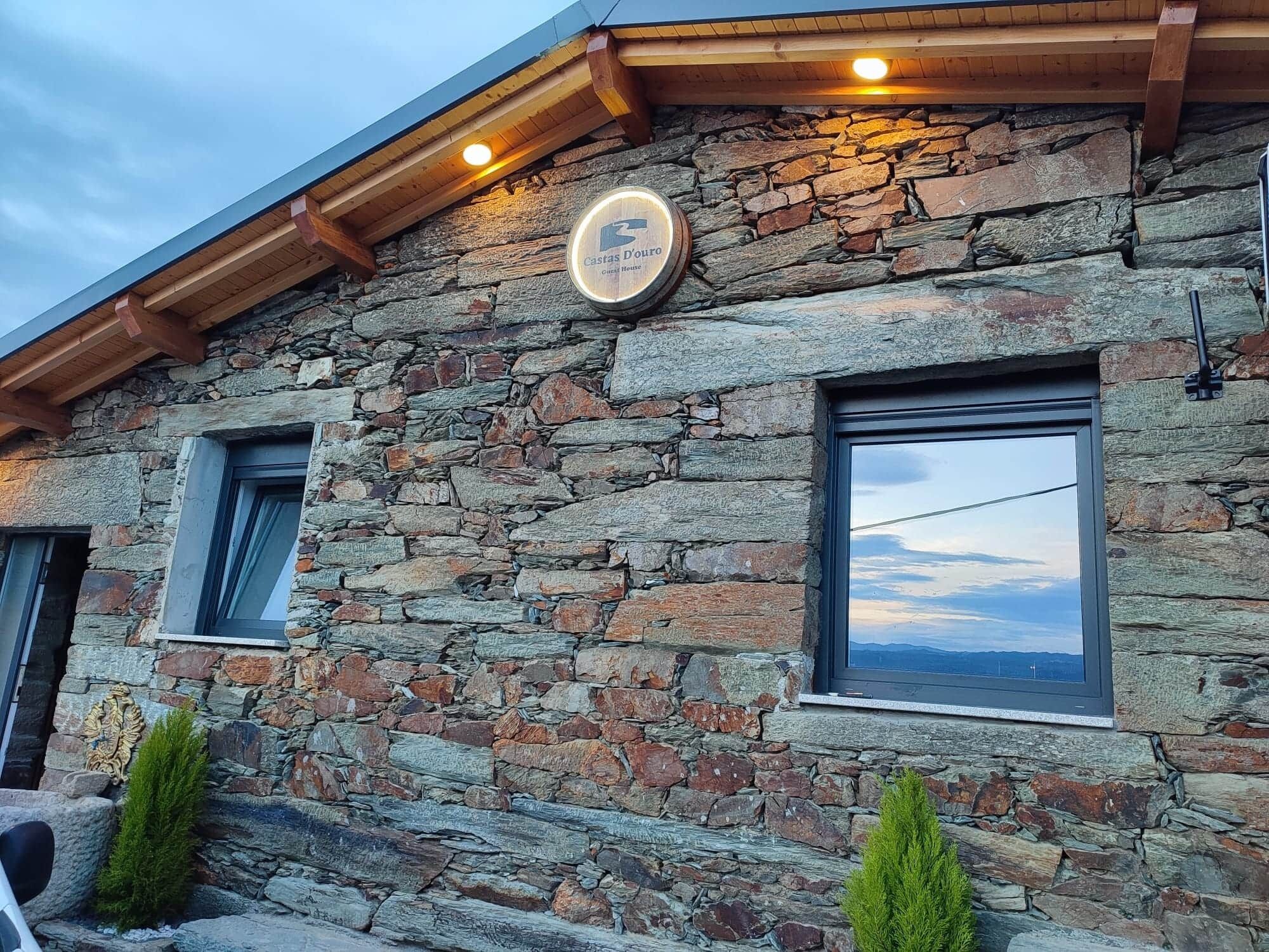 A stone building with a sign indicating it's a guest house. There are two windows, one with a view of the sky and the other with a landscape.