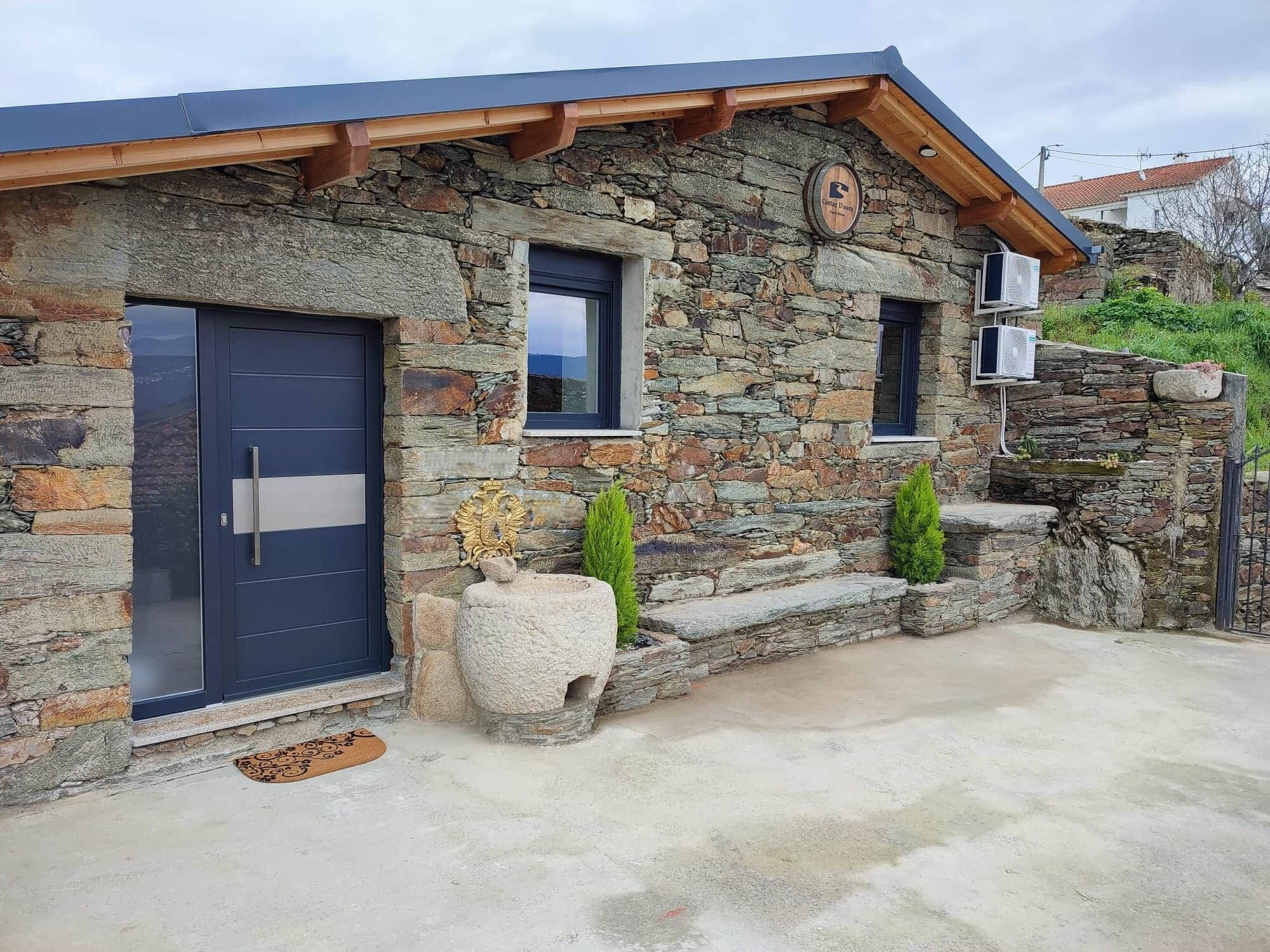 A stone building with a dark blue door, a small window, and a stone wall with a decorative element.
