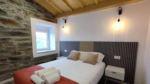 Una camera da letto con parete in pietra, soffitto in legno, un letto con poggiatesta a righe, due lampade da comodino e una finestra.