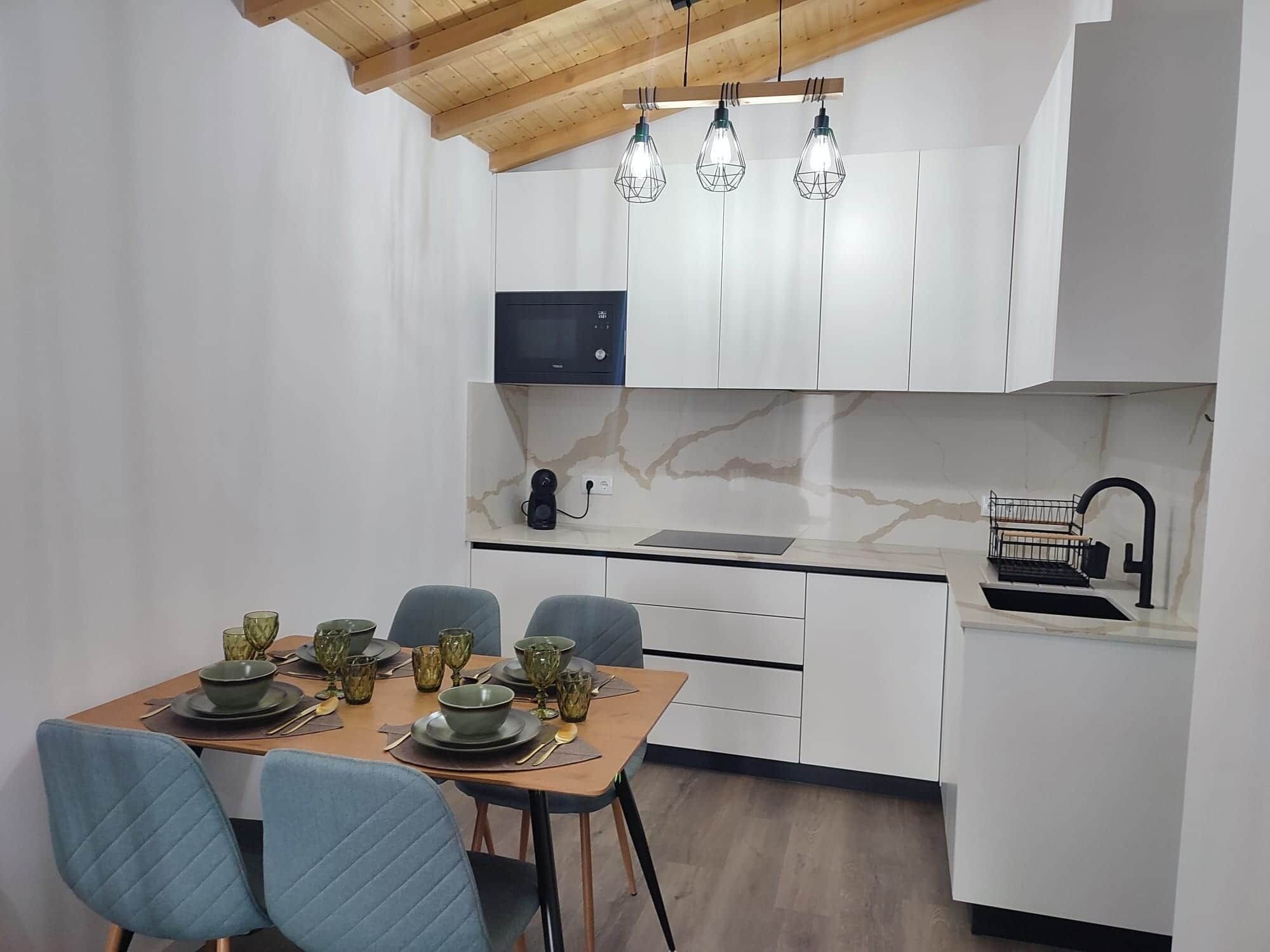A modern kitchen with white cabinets, a wooden ceiling, and a dining area with a table set for four.