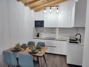 A modern kitchen with white cabinets, a wooden ceiling, and a dining area with a table set for four.