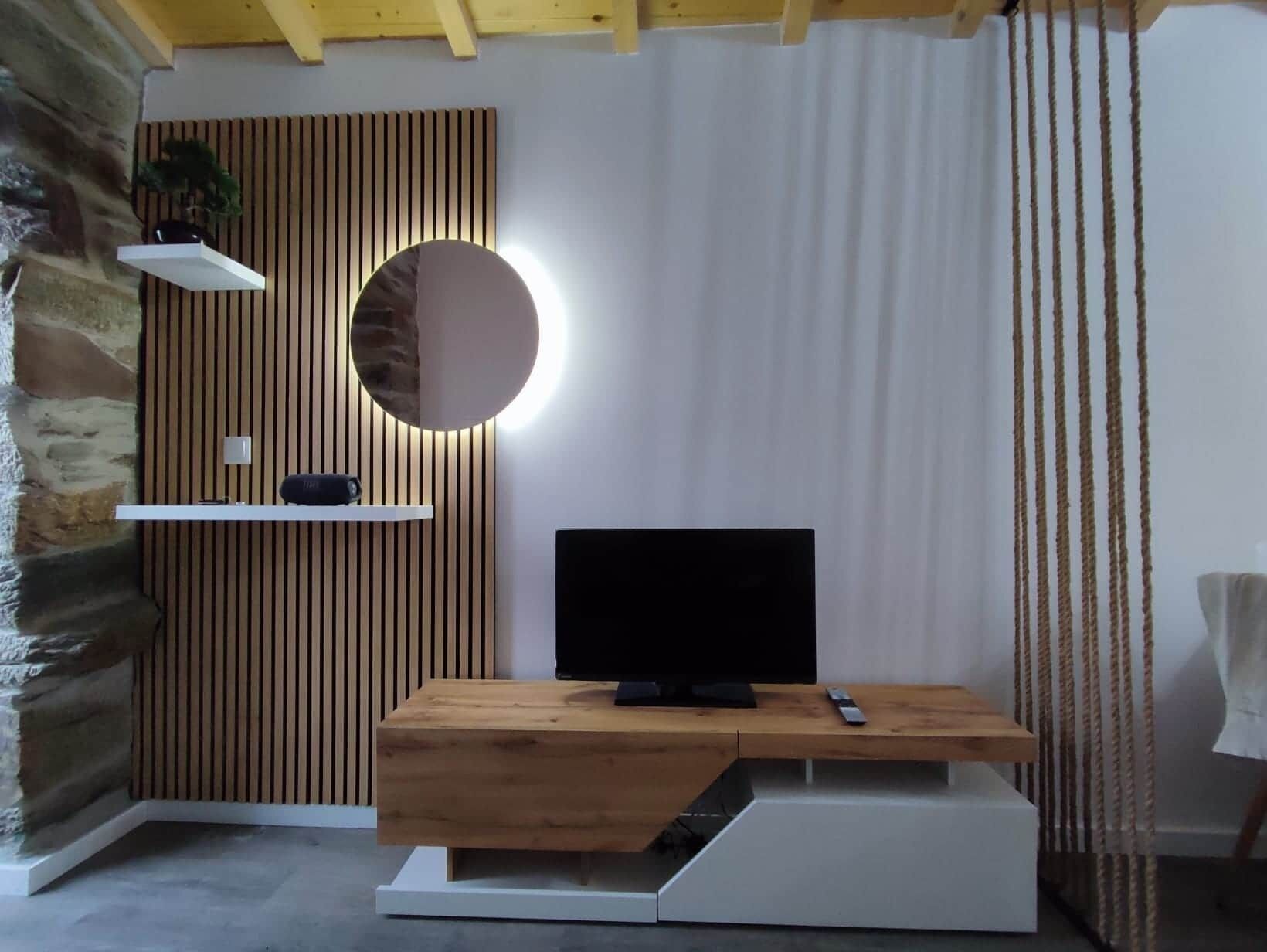 Ett modernt vardagsrum med en träinredd mediabänk, en platt-TV och en rund spegel.
