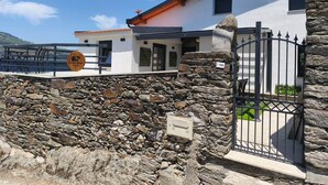 A stone wall with a metal gate, a white building with a red roof, and a wooden sign. - Castas D'ouro Guest House II (Casal de Loivos)