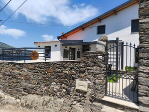 A stone wall with a metal gate, a white building with a red roof, and a wooden sign. - Castas D'ouro Guest House II (Casal de Loivos)