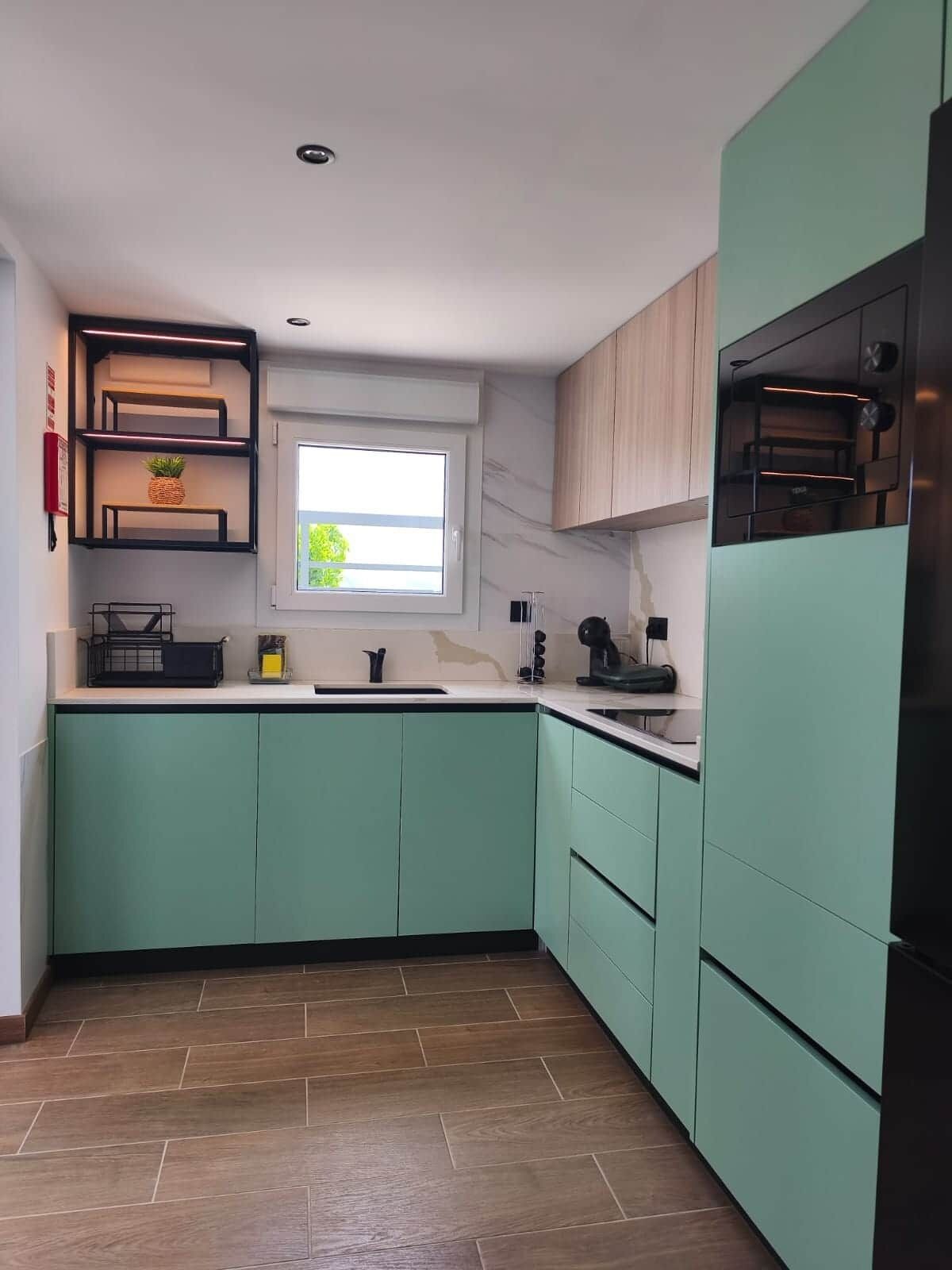 Une cuisine avec des armoires de couleur turquoise, une fenêtre et un four encastré.