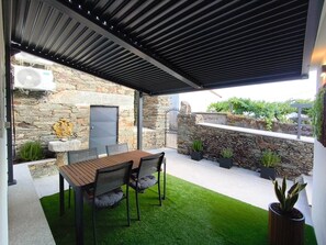 A covered patio with a stone wall, a wooden table with chairs, and potted plants. - Castas D'ouro Guest House II (Casal de Loivos)