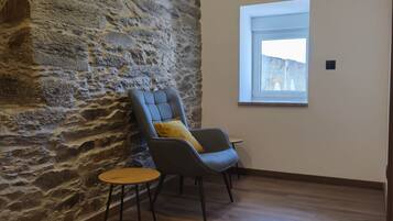 A room with a stone wall, a wooden floor, a window, and a chair with a small table.