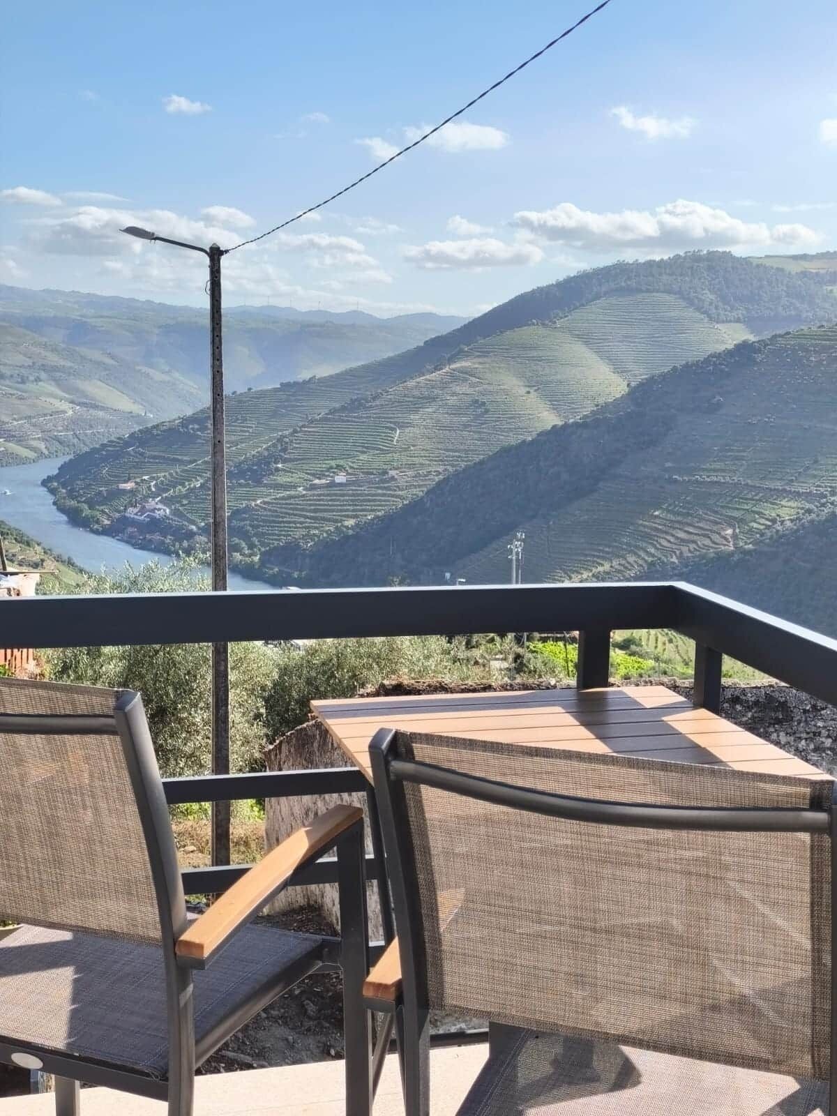 A terrace with two chairs and a table overlooking a valley with terraced fields and a river.