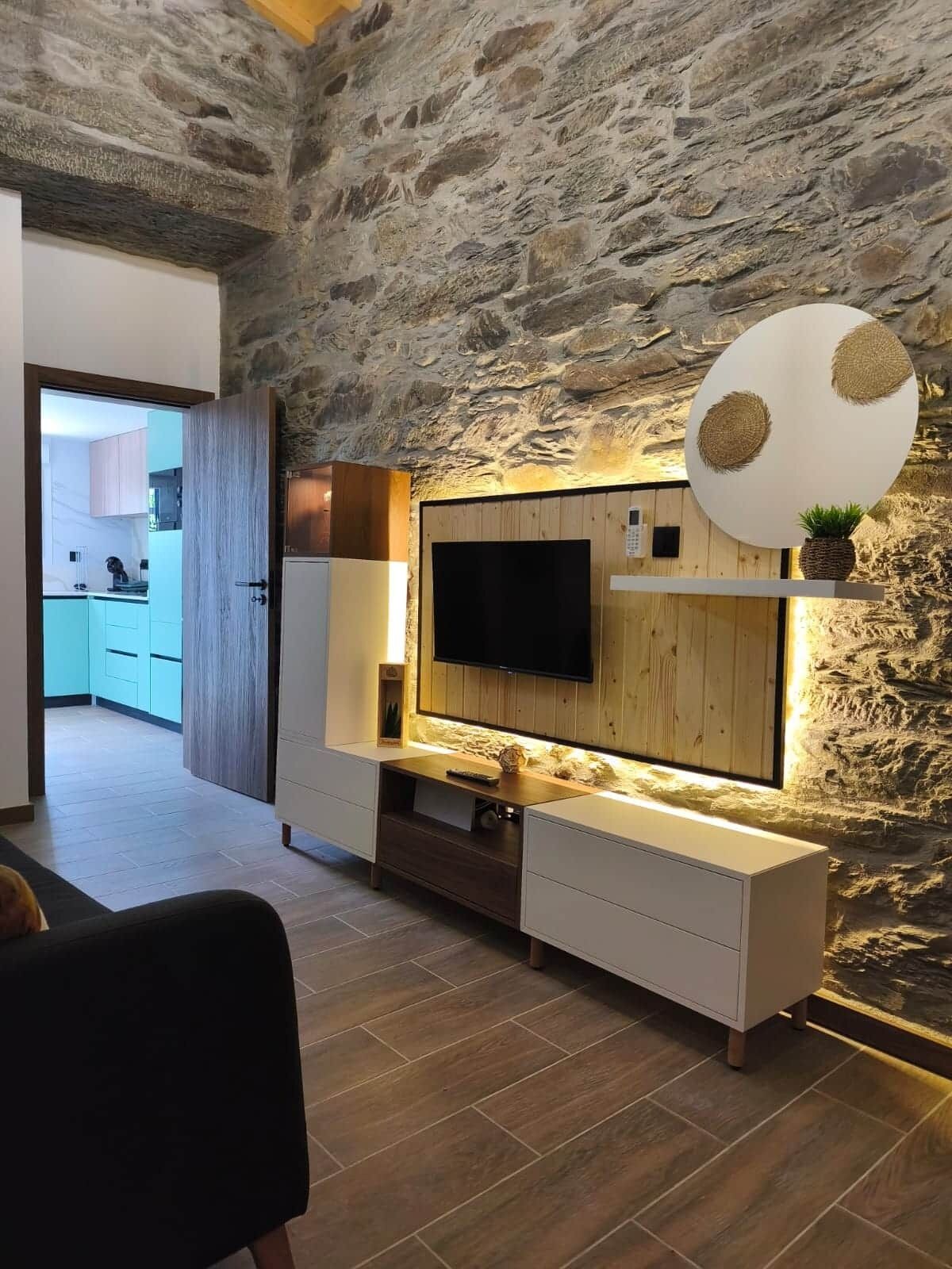 Een moderne woonkamer met een stenen muur, een hangende televisie en een houten tv-meubel.