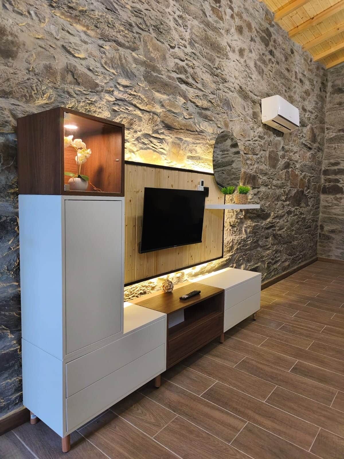 Een moderne woonkamer met een stenen muur, een wandgemonteerde televisie en ingebouwde houten kasten.
