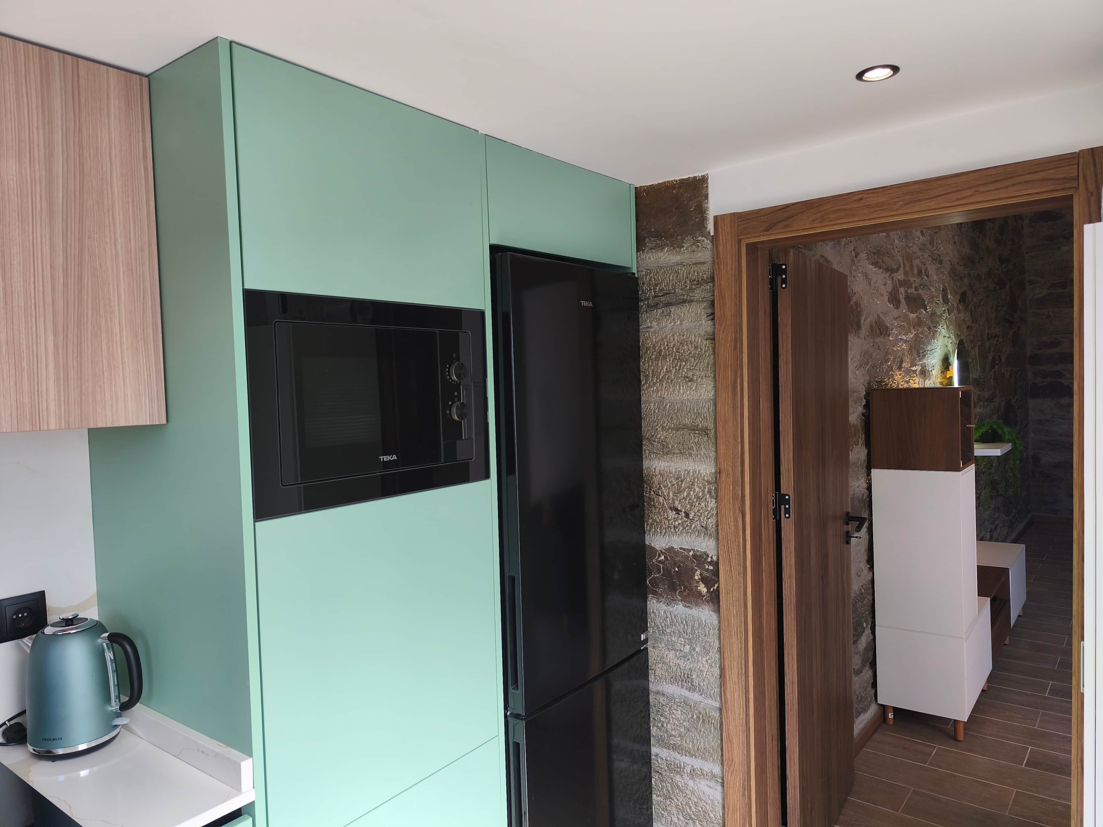 A kitchen with a black refrigerator, a microwave, and a kettle on the counter.