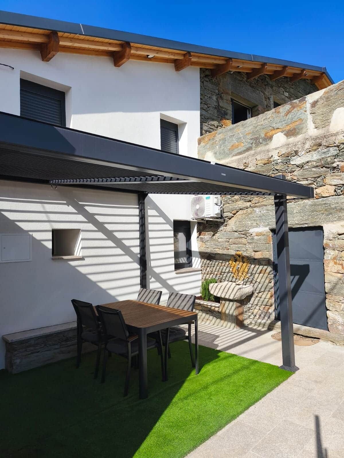 A patio with a table and chairs, a pergola, and a stone wall.