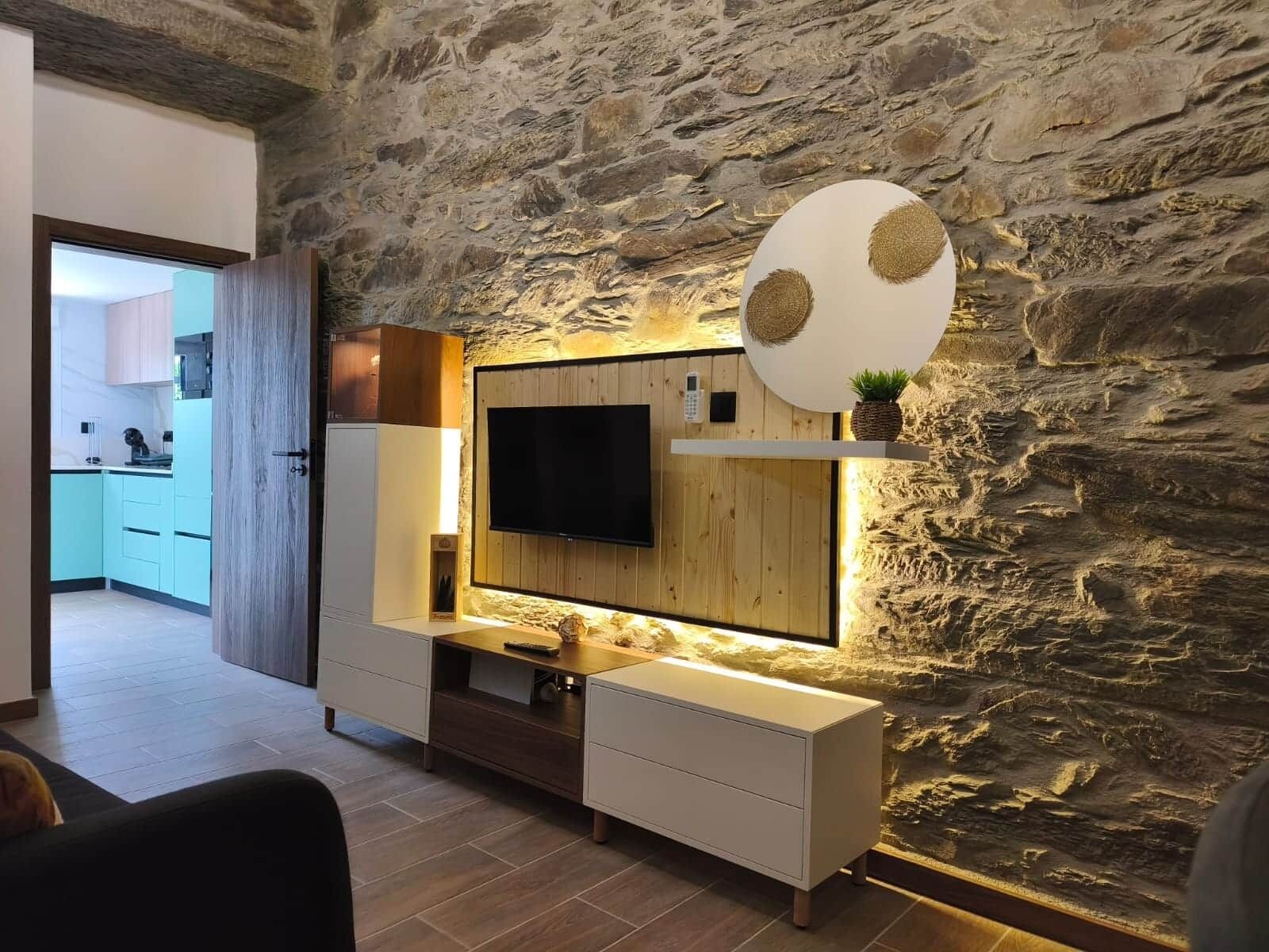 A modern living room with a stone wall, a mounted TV, and a minimalist entertainment unit.