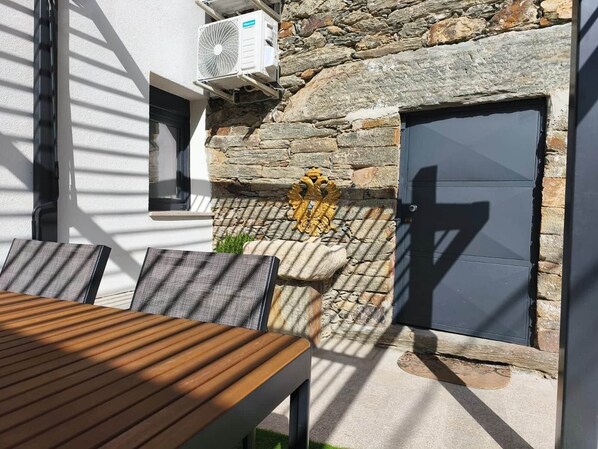 An outdoor seating area with a table and chairs, a stone wall, and a door.