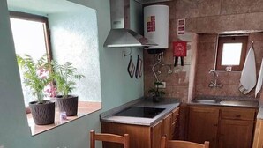 Ein Essbereich mit einem Holztisch, gedeckt für vier Personen, eine Küche mit Gasherd und ein Fenster mit einer Pflanze.