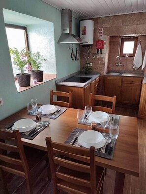 Zona pranzo con tavolo in legno apparecchiata per quattro, cucina con piano cottura a gas e una finestra con una pianta.
