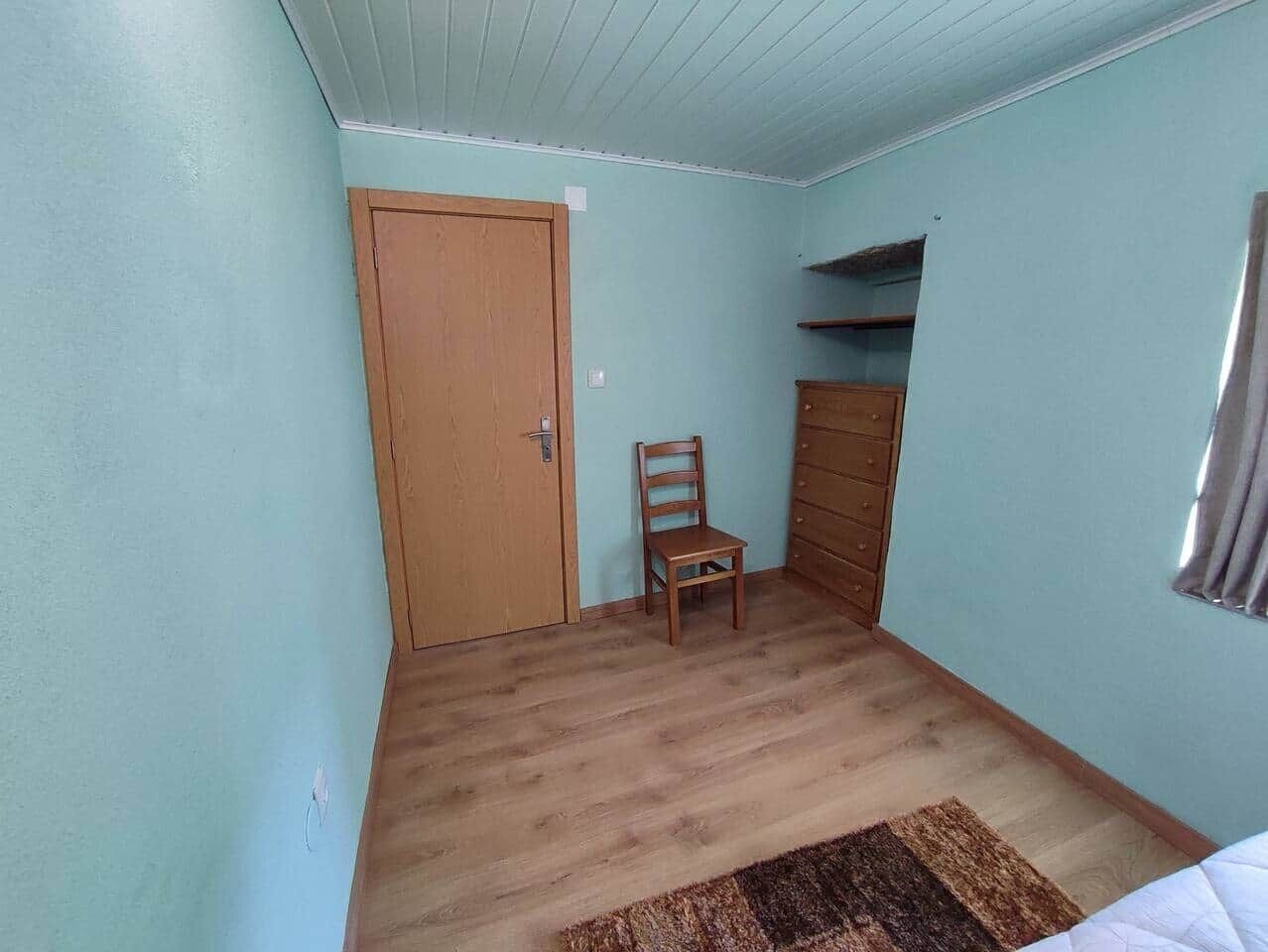 A room with a wooden door, a chair, a dresser, and a window with curtains.