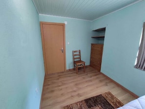 A room with a wooden door, a chair, a dresser, and a window with curtains.