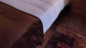Ein ordentlich bezogenes Bett mit einem Holzkopfstück, zwei Nachttische mit Lampen und eine braune Decke auf dem Boden.