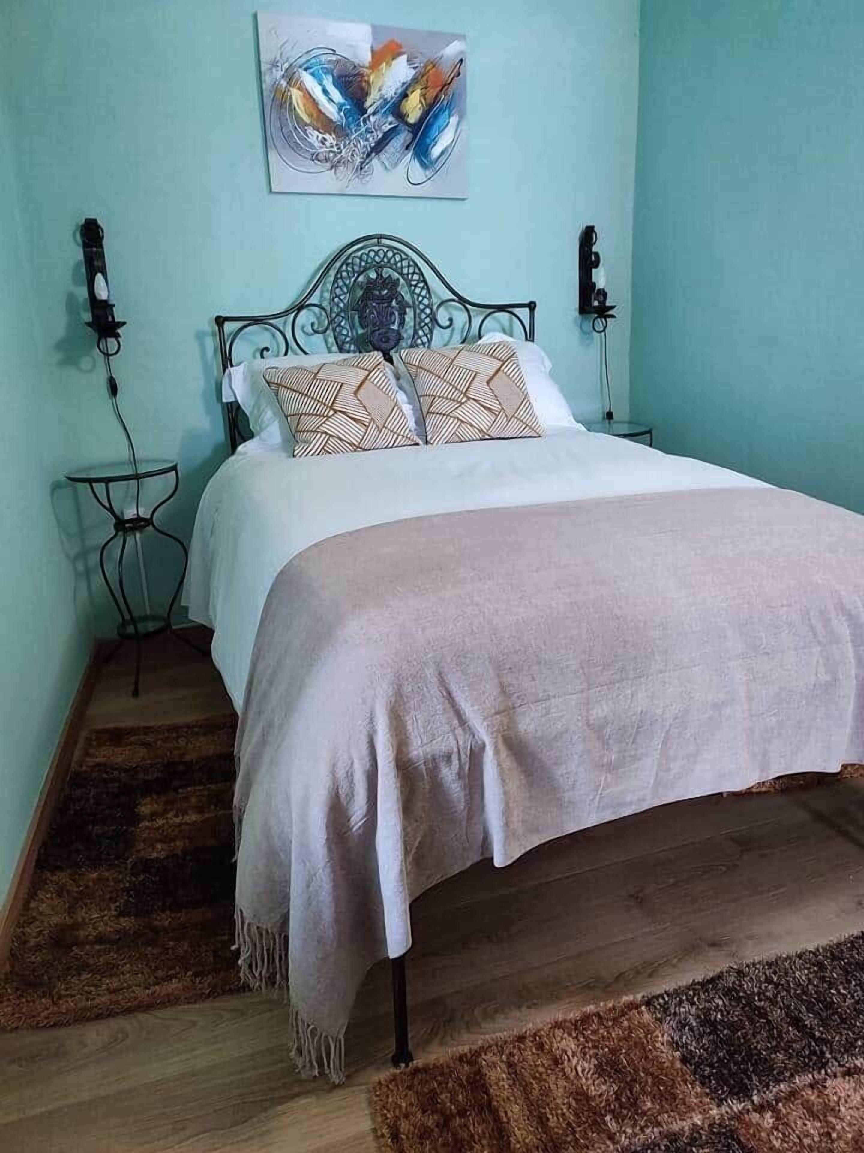 Una cama con un cojín estampado, una mesita de noche y una obra de arte colgada en la pared.